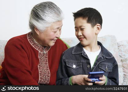 Close-up of a boy sitting with his grandmother holding a video game console