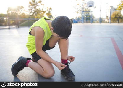 Close-up of a boy tying his shoelaces on an urban basketball court at sunset.