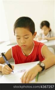 Close-up of a boy writing in a spiral notebook in the classroom