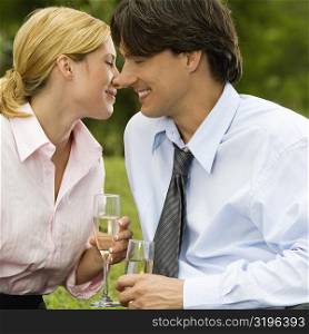 Close-up of a businessman and a businesswoman sitting in the park holding champagne flutes