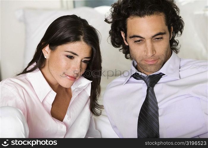 Close-up of a businessman and a businesswoman sitting on the bed looking down