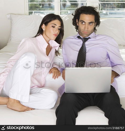 Close-up of a businessman and a businesswoman sitting on the bed using a laptop