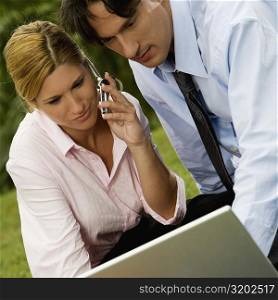 Close-up of a businessman and a businesswoman working on a laptop and talking on a mobile phone