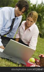 Close-up of a businessman and a businesswoman working on a laptop in the park