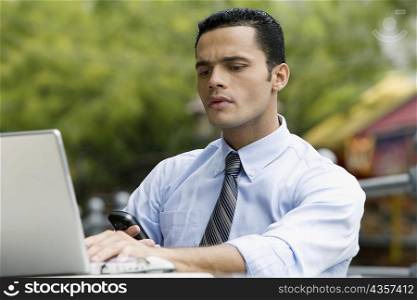 Close-up of a businessman checking his phone while using a laptop