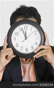 Close-up of a businessman hiding his face with a clock