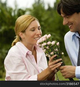 Close-up of a businessman holding a bunch of flowers with a businesswoman smelling them