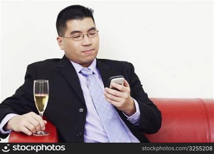 Close-up of a businessman holding a champagne flute and operating a mobile phone