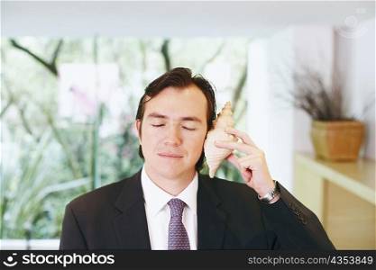 Close-up of a businessman holding a shell close to his ear