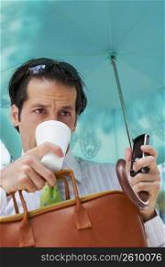 Close-up of a businessman holding an umbrella and drinking cold drink