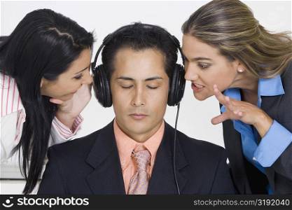 Close-up of a businessman listening to music while two businesswomen bothering him