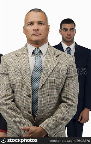 Close-up of a businessman looking serious with two businessmen standing behind him