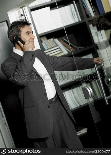Close-up of a businessman opening a glass door and talking on a mobile phone