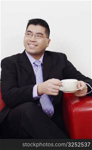 Close-up of a businessman sitting on a couch with a cup of tea and smiling