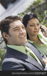 Close-up of a businessman smiling with a businesswoman talking on a mobile phone
