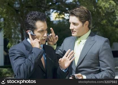Close-up of a businessman talking on a hands free device with another businessman standing beside him