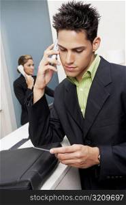 Close-up of a businessman talking on a mobile phone and a receptionist talking on the phone in the background