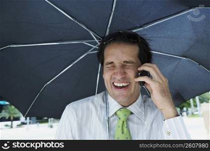 Close-up of a businessman talking on a mobile phone under an umbrella