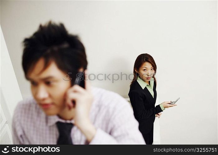Close-up of a businessman talking on a mobile phone with a businesswoman standing in the background