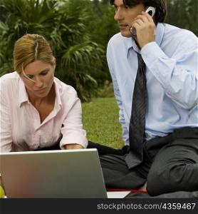 Close-up of a businessman talking on a mobile phone with a businesswoman using a laptop