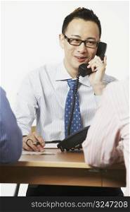 Close-up of a businessman talking on the telephone with two businessmen sitting in front of him