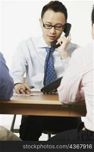 Close-up of a businessman talking on the telephone with two businessmen sitting in front of him