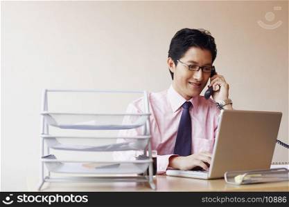 Close-up of a businessman using a laptop and talking on the telephone