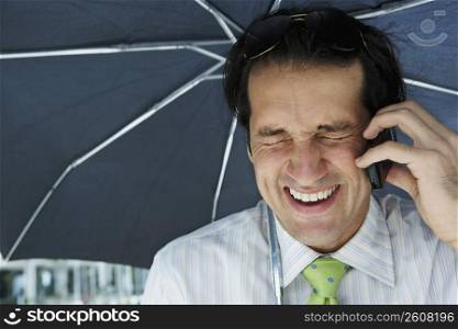 Close-up of a businessman using a mobile phone under an umbrella
