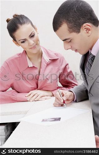 Close-up of a businessman writing on paper with a businesswoman standing beside him
