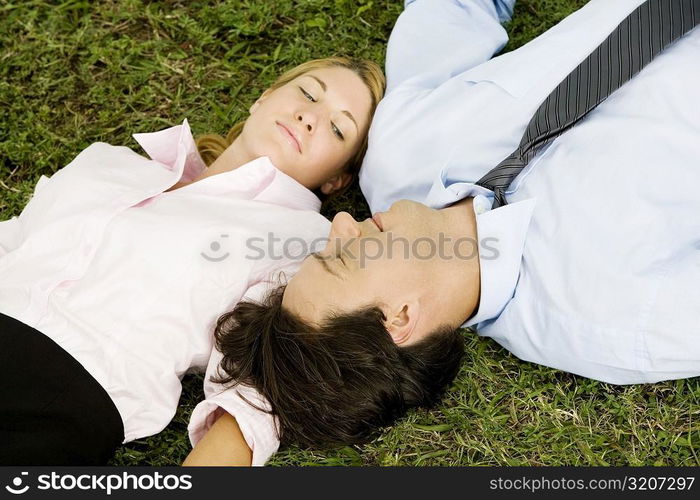 Close-up of a businesswoman and a businessman lying on the grass