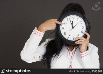 Close-up of a businesswoman holding a clock in front of her face and pointing
