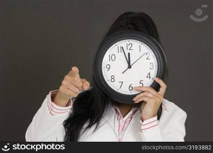 Close-up of a businesswoman holding a clock in front of her face and pointing