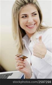 Close-up of a businesswoman holding a credit card and showing a thumbs up sign