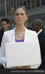 Close-up of a businesswoman holding a laptop with two businessmen standing behind her