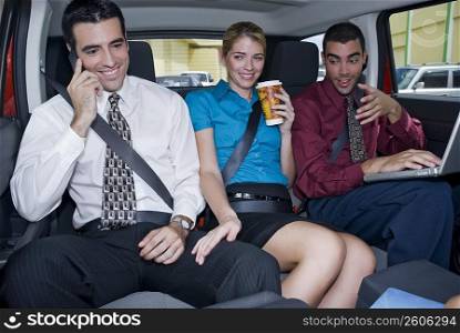 Close-up of a businesswoman sitting between two businessmen in a car and smiling
