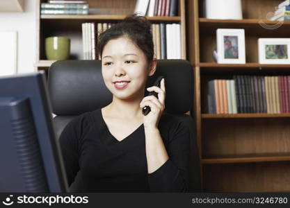 Close-up of a businesswoman sitting in front of a computer monitor using a mobile phone