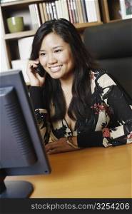 Close-up of a businesswoman sitting in front of a computer monitor using a mobile phone