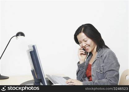 Close-up of a businesswoman sitting in front of a computer using a mobile phone