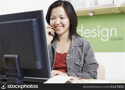 Close-up of a businesswoman sitting in front of a computer using a mobile phone