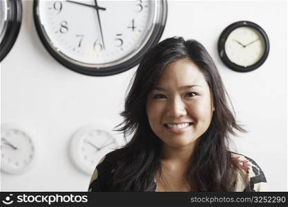 Close-up of a businesswoman smiling standing in front of clocks on the wall