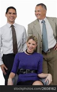Close-up of a businesswoman smiling with two businessmen standing behind her