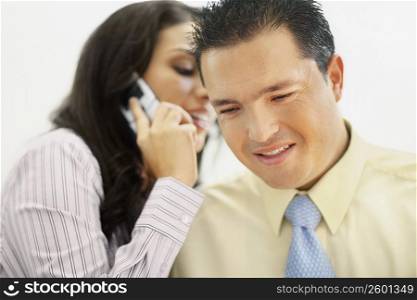 Close-up of a businesswoman talking on a flip phone and whispering to a businessman