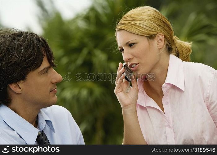 Close-up of a businesswoman talking on a mobile phone with a businessman looking at her