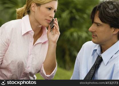 Close-up of a businesswoman talking on a mobile phone with a businessman looking at her