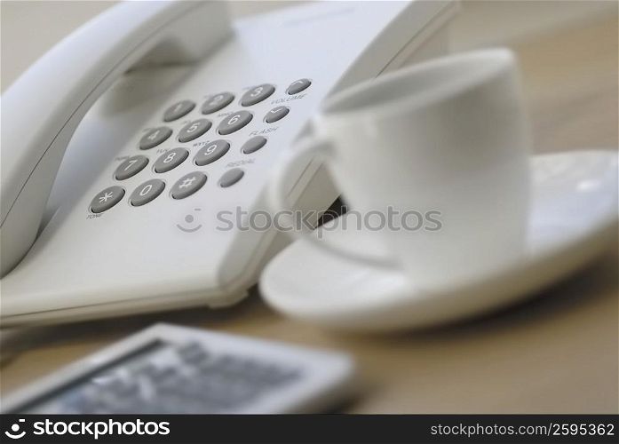 Close-up of a calculator and a tea cup near a telephone
