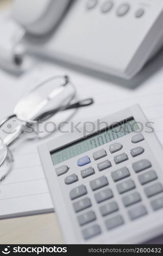 Close-up of a calculator and eyeglasses in front of a telephone