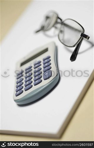 Close-up of a calculator with a pair of eyeglasses on a notepad