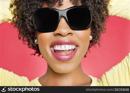 Close-up of a cheerful African American woman wearing sunglasses over colored background