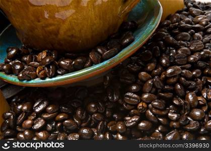 Close up of a coffee mug and saucer overflowing with dark roasted coffee beans. Shallow depth of field.
