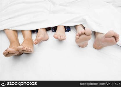 Close-up of a couple&acute;s feet with their child on the bed